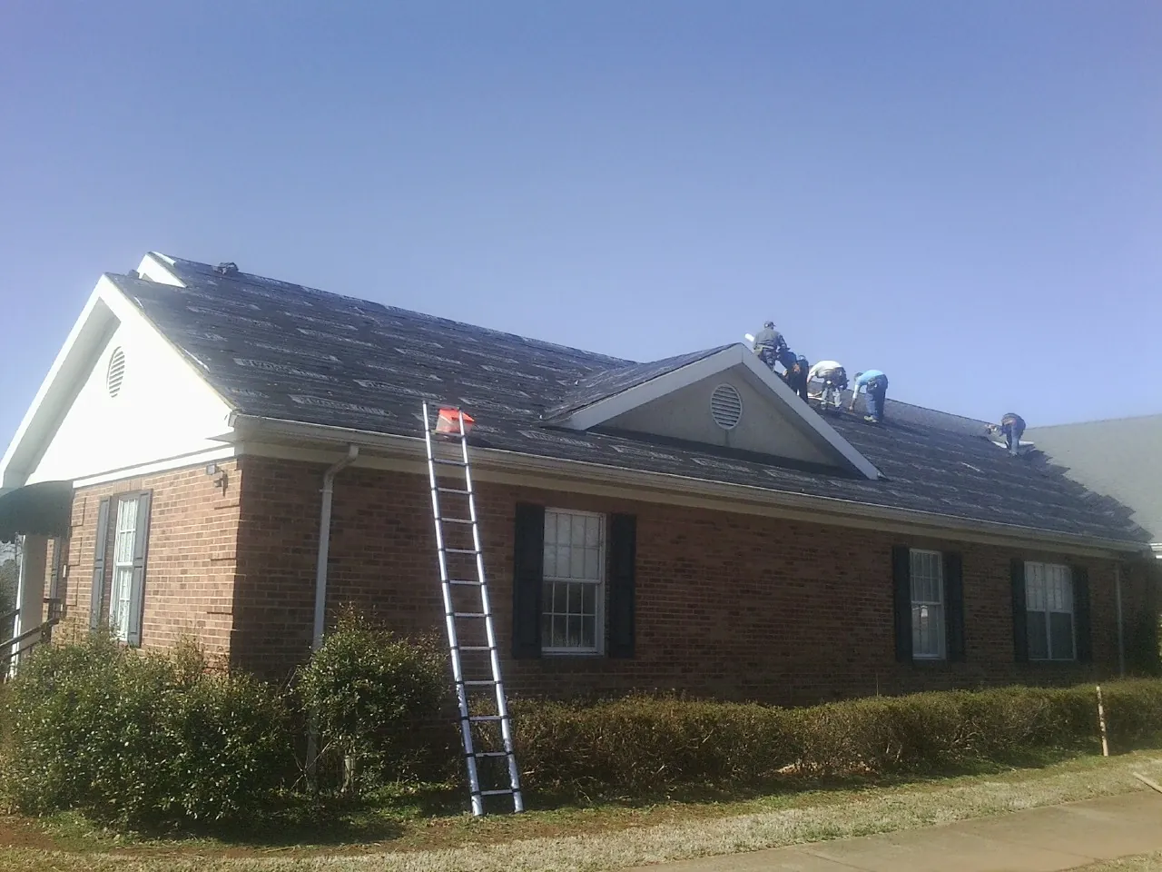 Crew tearing shingles off a brick ranch roof with a ladder set — Metal Roof Repair work by our crew in Orleans