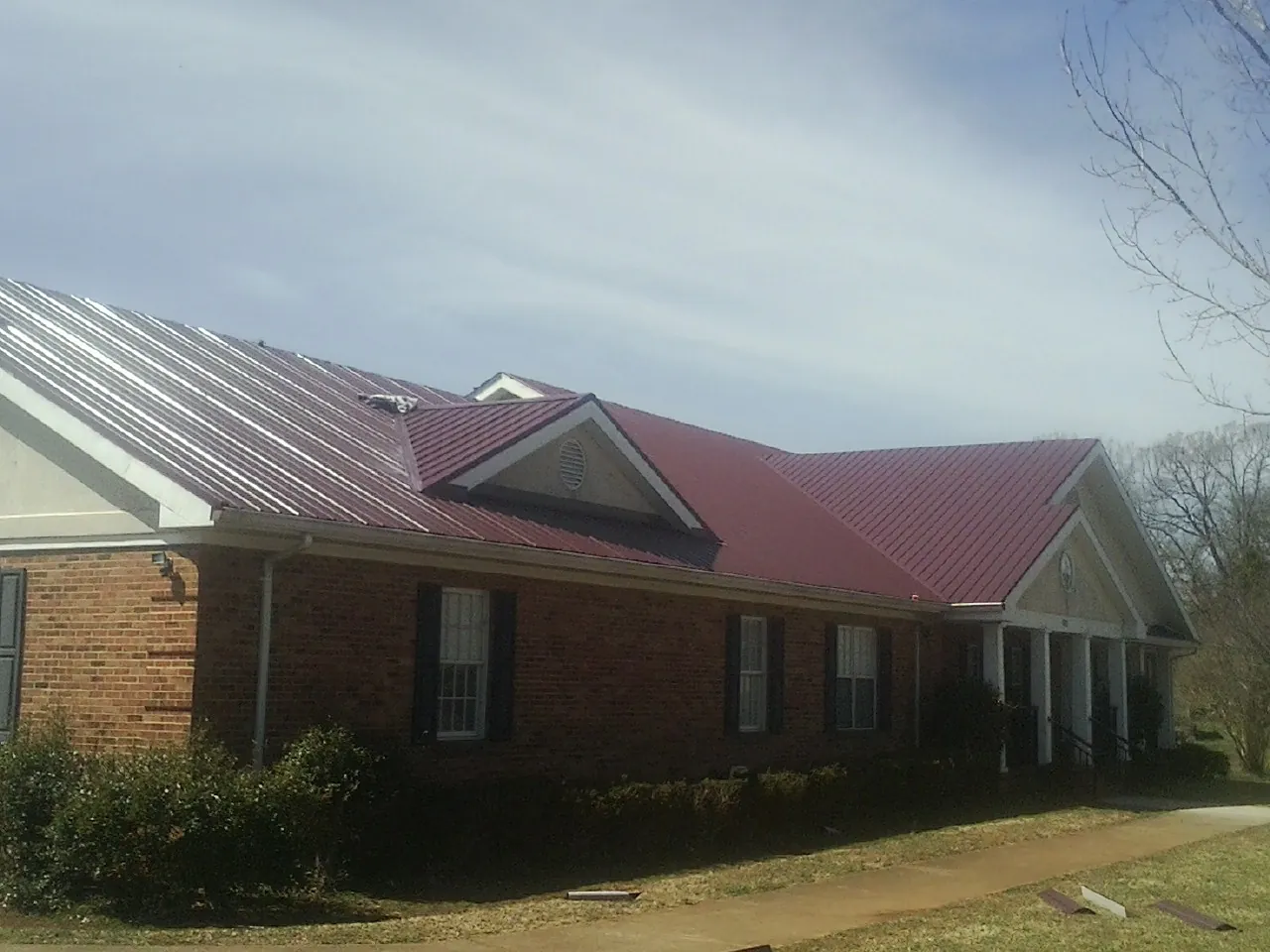 Red metal roof with gabled entries on a long brick building, from a Hail Damage Roof Repair job in Orleans