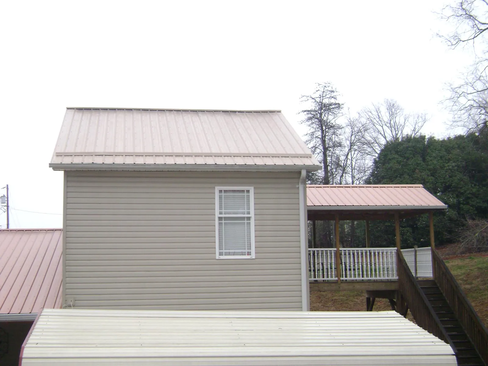 Tan metal roofs on a two story addition and attached porch, from a Roof Replacement job in Orleans